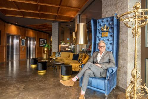 a man sitting in a blue chair in a room at KING's Hotel First in Munich