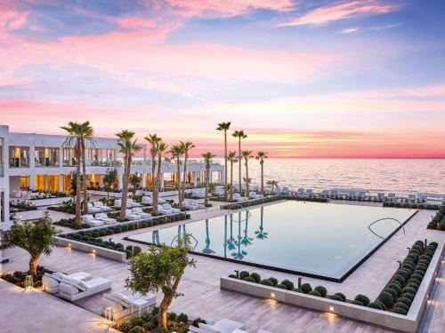 un'immagine di una piscina del resort con palme e l'oceano di Grecotel LUX.ME White Palace​ ad Adelianos Kampos