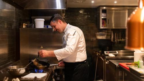 a man in a kitchen preparing food on a stove at Hôtel - Restaurant Le Globe in Meursault