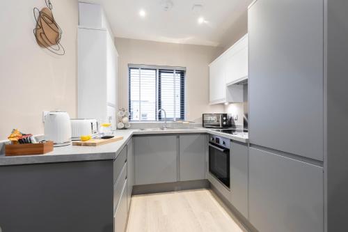 una cocina con armarios blancos y electrodomésticos de acero inoxidable en Elliot Oliver - Chic 2 Bedroom Town Centre Apartment en Cheltenham