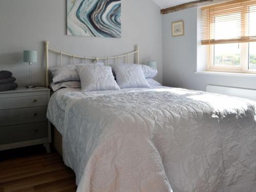 a bedroom with a bed with a white comforter and a window at The Old Cow Shed in Wickwar