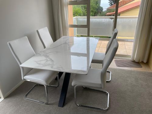 a glass table and two white chairs in front of a window at Orewa Beach Apartment in Auckland