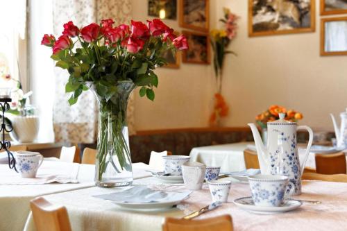 eine Vase mit Blumen auf einem Tisch mit Teller und Tassen in der Unterkunft Pension Wiesengrund in Neuschönau