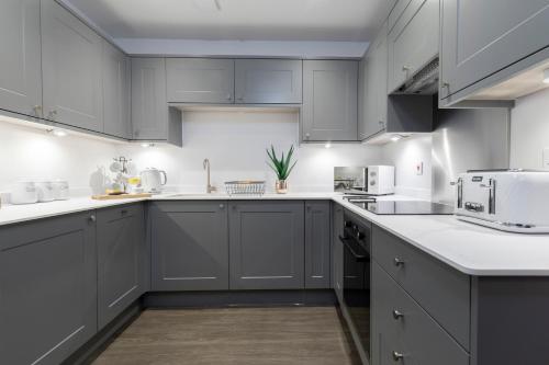 uma cozinha com armários cinzentos e bancadas brancas em Elliot Oliver - Luxury 2 Bedroom Regency Apartment With Parking & EV Charger em Cheltenham