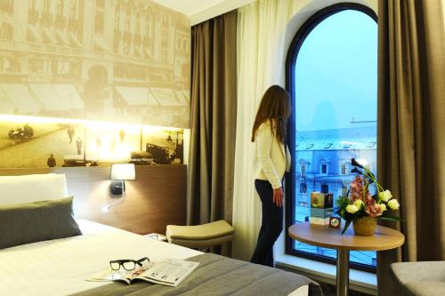 a woman standing in a hotel room looking out the window at Mercure Bucharest City Center in Bucharest