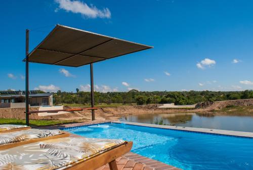 ein Pool mit einem großen Regenschirm neben einem Wasserkörper in der Unterkunft Casa de la Presa 4 in Polokwane