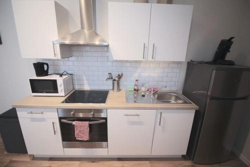 a kitchen with white cabinets and a sink and a microwave at Charmant appart 2 ch avec terrasse en centre ville in Liège