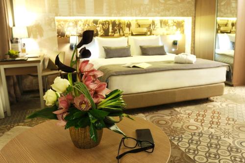 a bedroom with a bed and a table with a vase of flowers at Mercure Bucharest City Center in Bucharest