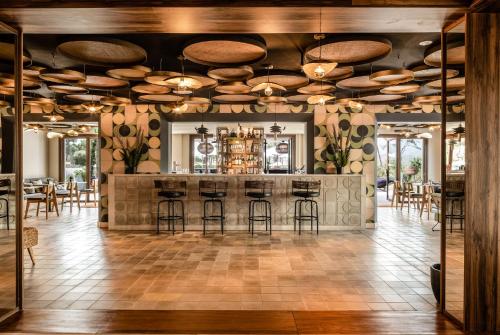 a room with a bar with stools and tables at Kimpton Aysla Mallorca, an IHG Hotel in Santa Ponsa