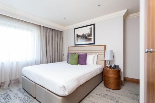 a bedroom with a large white bed with purple and green pillows at Sanctum Maida Vale in London