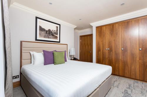 a bedroom with a large bed with purple and green pillows at Sanctum Maida Vale in London
