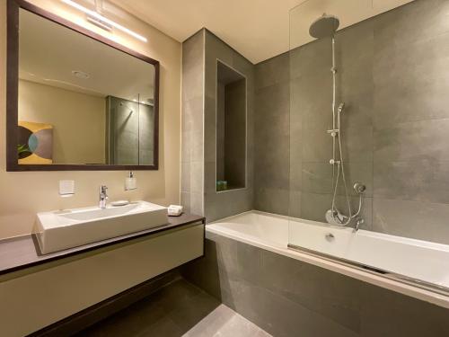 a bathroom with a sink and a tub and a mirror at WelHome - Evergreen Apartment Amidst Vibrant JVC With Pool in Dubai