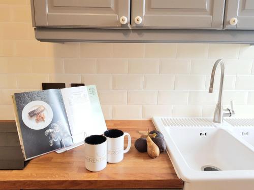 un mostrador de cocina con 2 tazas de café y un libro en Caman House Apt 2 - by Where Stags Roar en Newtonmore