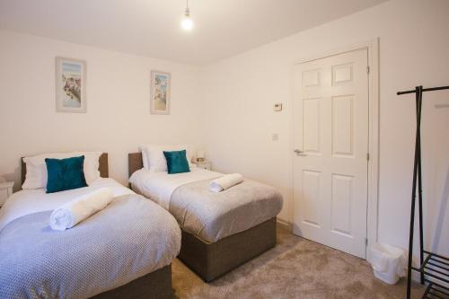 2 letti in una camera con pareti bianche e cuscini blu di Cosy 2-bed home - For Company contractor and Leisure stays - NEC, Airport, HS2, Contractors, Resort World a Marston Green