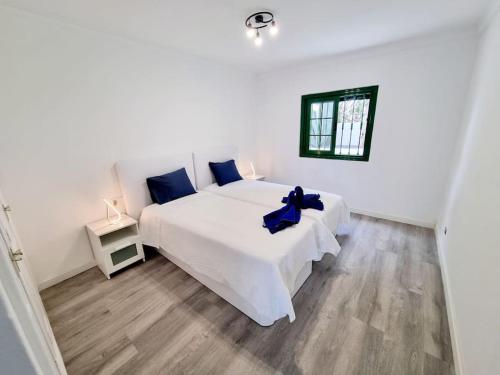 a white bedroom with a large white bed with blue pillows at Playa Bastian first line of the sea in Costa Teguise