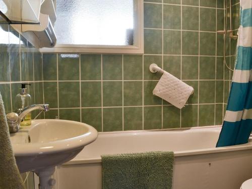 a green tiled bathroom with a sink and a tub at Gwyrfai Cottage in Waenfawr