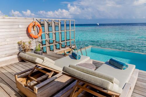 a deck with chairs and a swimming pool next to the ocean at Kagi Maldives Resort & Spa in North Male Atoll