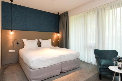 a bedroom with a large white bed and a chair at Hotel De Roode Schuur in Nijkerk