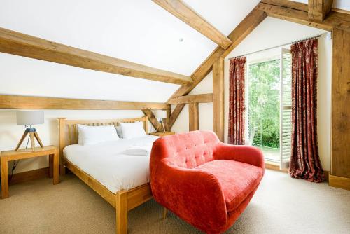 um quarto com uma cama e uma cadeira vermelha em Lakeside property with hot tub Barn Owl HM08 em Somerford Keynes