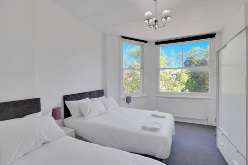 two beds in a white room with two windows at Hamilton Apartments hosted by Maysa London in London