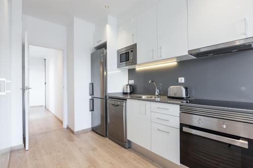 uma cozinha com armários brancos e um frigorífico de aço inoxidável em Bright Apartment with Balconies em Barcelona