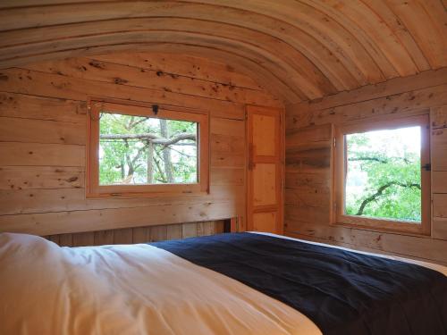 a bedroom in a log cabin with two windows at Cabane perchée - Les Cabanes de Fallot - sauna bain-froid piscine in LʼIsle-Bouzon