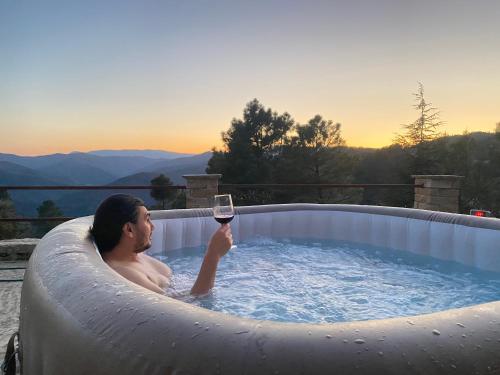 a man in a hot tub with a glass of wine at Maison des Monts Bleus in Saint-Roman-de-Tousque