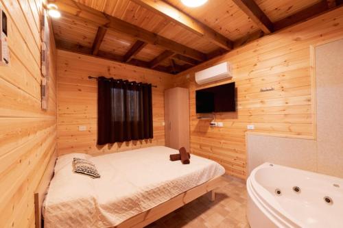 a bedroom with a bed and a tub in a wooden room at צמרת הצימרים - מתחם צימרים מקסים עם בריכה במתחם וג'קוזי פרטי - Vacation complex with heated pool and private jacuzzi in Dāliyat el Karmil