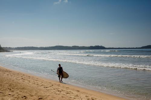 a man walking on the beach with a surfboard at W15 Weligama in Weligama