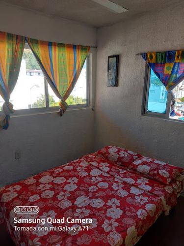 a bedroom with a bed with a red bedspread and two windows at Hotel la Quebrada in Acapulco