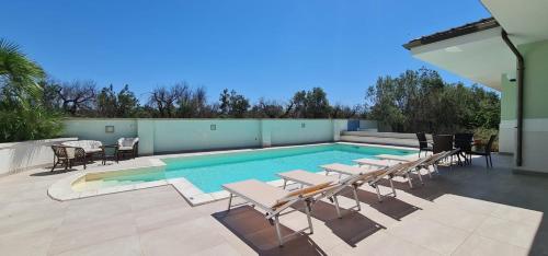 a swimming pool with tables and chairs next to at Villa Vimade con Piscina Privata in Marina di Mancaversa