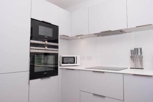 a white kitchen with a tv and a microwave at 4 Rockham - Luxury Apartment at Byron Woolacombe, only 4 minute walk to Woolacombe Beach! in Woolacombe