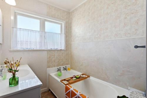 uma casa de banho com uma banheira, um lavatório e uma janela em Retro Cottage in Opotiki CBD em Opotiki