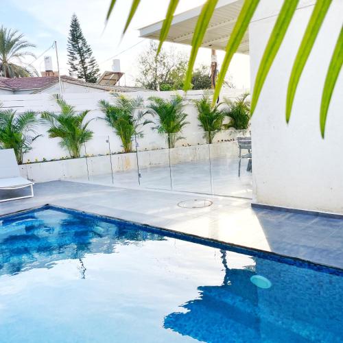 a swimming pool in front of a house with palm trees at Luz Mansion ~ Lux & Comfy in Rishon LeẔiyyon