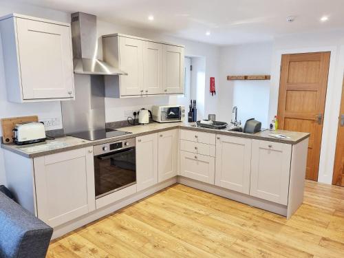 a kitchen with white cabinets and a wooden floor at Berts Bothy in Threlkeld