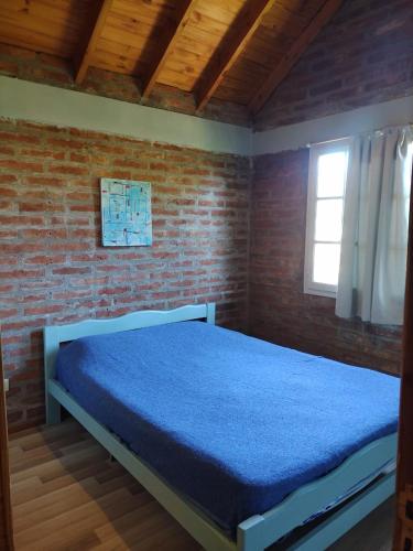 1 dormitorio con 1 cama azul en una pared de ladrillo en Cabaña Fuego Interior en El Bolsón