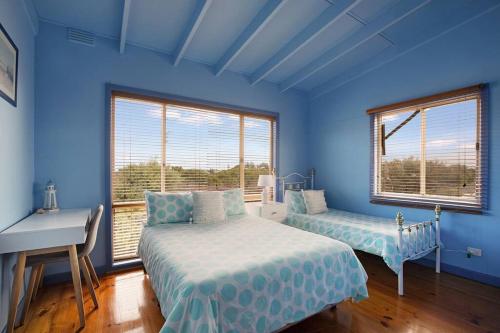 a blue bedroom with two beds and a desk and windows at Family Retreat 500m to the beach in Ocean Grove