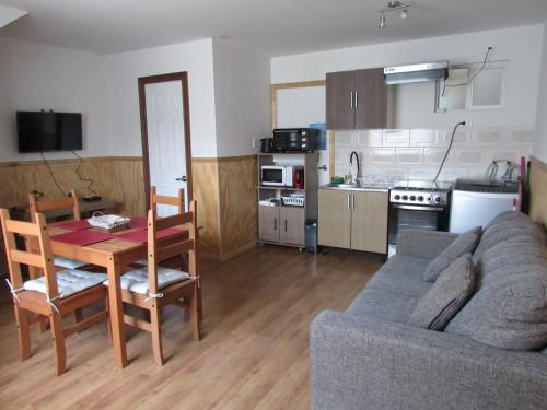 ein Wohnzimmer mit einem Sofa und einem Tisch sowie eine Küche in der Unterkunft Departamentos Kitkaika in Punta Arenas