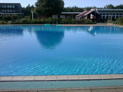 a large pool of blue water with a house in the background at Heidehotel Herrenbrücke in Faßberg