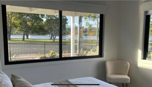 a bedroom with two windows and a bed and a chair at 4BR Waterfront - Skippers Quarterdeck in Lakes Entrance