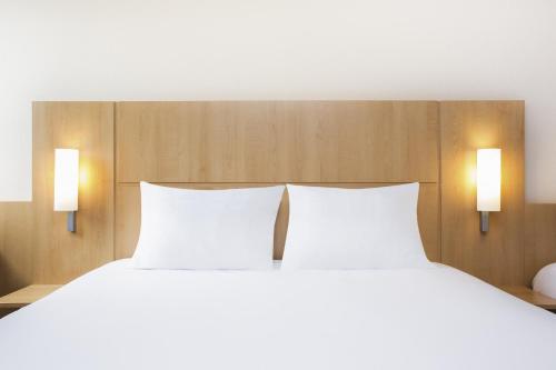 a bed with two white pillows and two lights at ibis Charleville Mézières in Villers-Semeuse