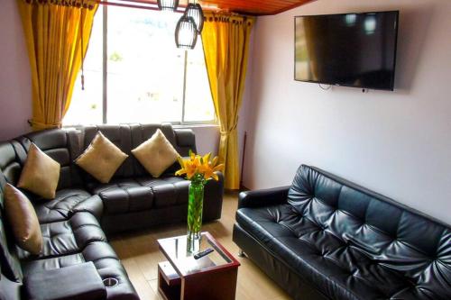 sala de estar con sofá de cuero negro y TV en Apartamento en el Centro de Paipa, en Paipa