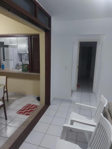 a living room with two white chairs and a kitchen at Apartamento em guarajuba 200m da praia in Camaçari