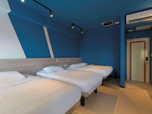 três camas num quarto com uma parede azul em ibis budget Phnom Penh Riverside em Phnom Penh