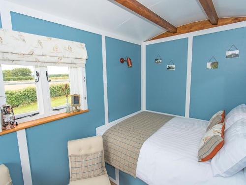 a bedroom with blue walls and a bed and a window at Jill Hoot-uk36796 in Foulsham