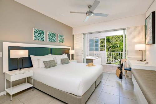 a bedroom with a large white bed and a balcony at Peppers Beach Club in Port Douglas
