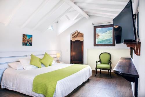 a white bedroom with a bed and a green chair at Hotel y Spa Getsemani in Villa de Leyva