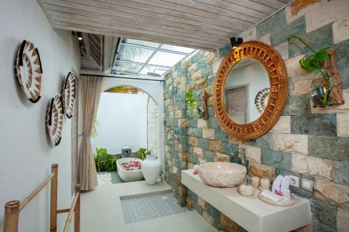 baño con espejo y pared de piedra en Amaya Sebatu Villa, en Ubud