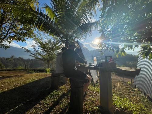 two people sitting at a table under a palm tree at Monsonkeang Camping view ม่อนสันเกี๋ยง in Mae Chaem