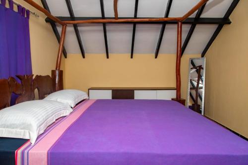 a bedroom with a large bed with purple sheets at MY SUN V.I.P COTTAGE @ KARIBU PALMS RESORT in Diani Beach